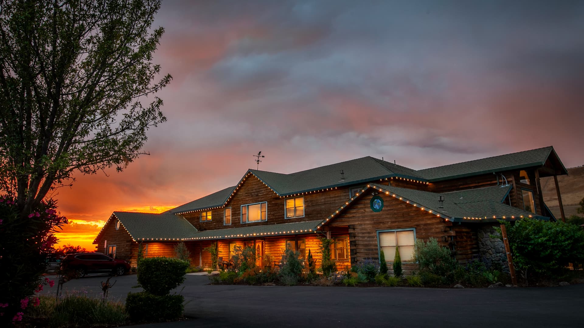 Exterior of inn, lights on roof edge, sunset and trees