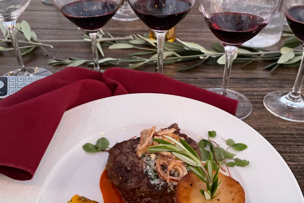 A gourmet steak dish garnished with fresh herbs, accompanied by red wine glasses and a stylish table setting.