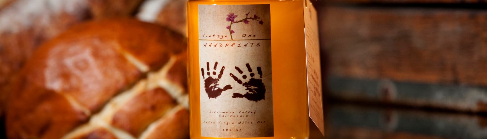 A bottle of extra virgin olive oil with a label featuring handprints, placed near a loaf of bread.