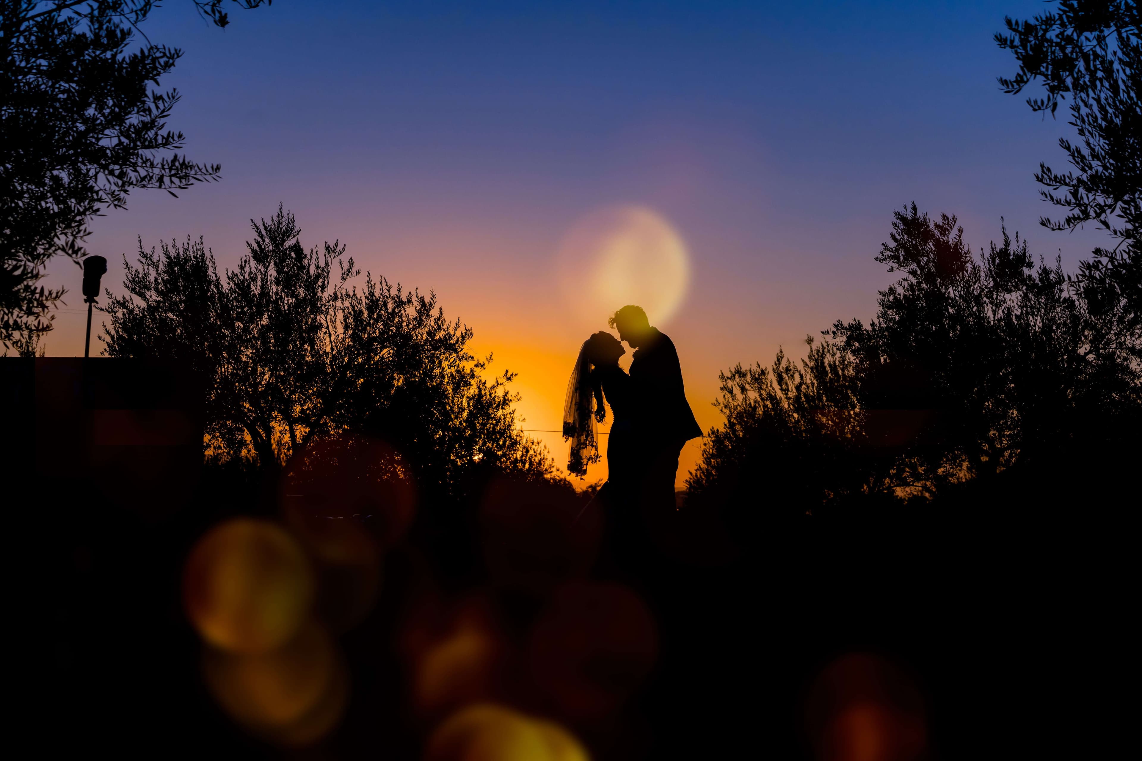 A couple embraces in silhouette against a vibrant sunset.