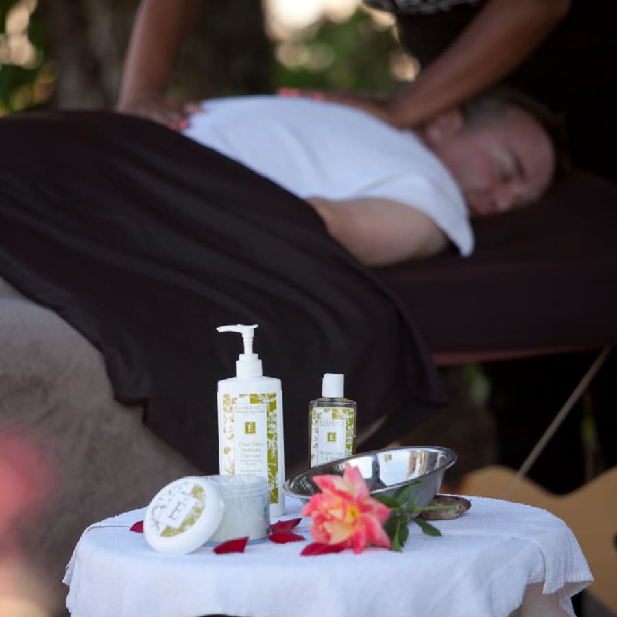 A person receives a massage while spa products and a flower are displayed on a table nearby.