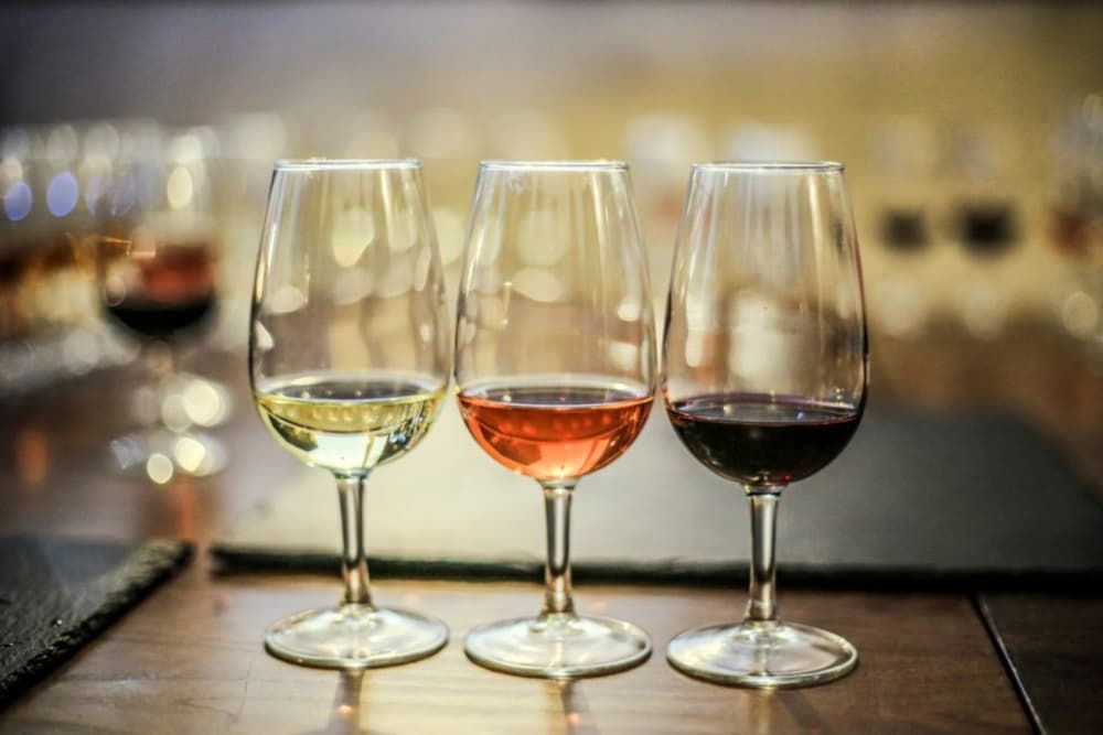 Three wine glasses filled with white, rosé, and red wine are arranged on a table.