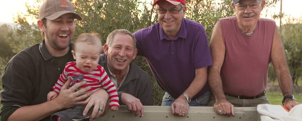 A group of four men and a baby smiling outdoors.