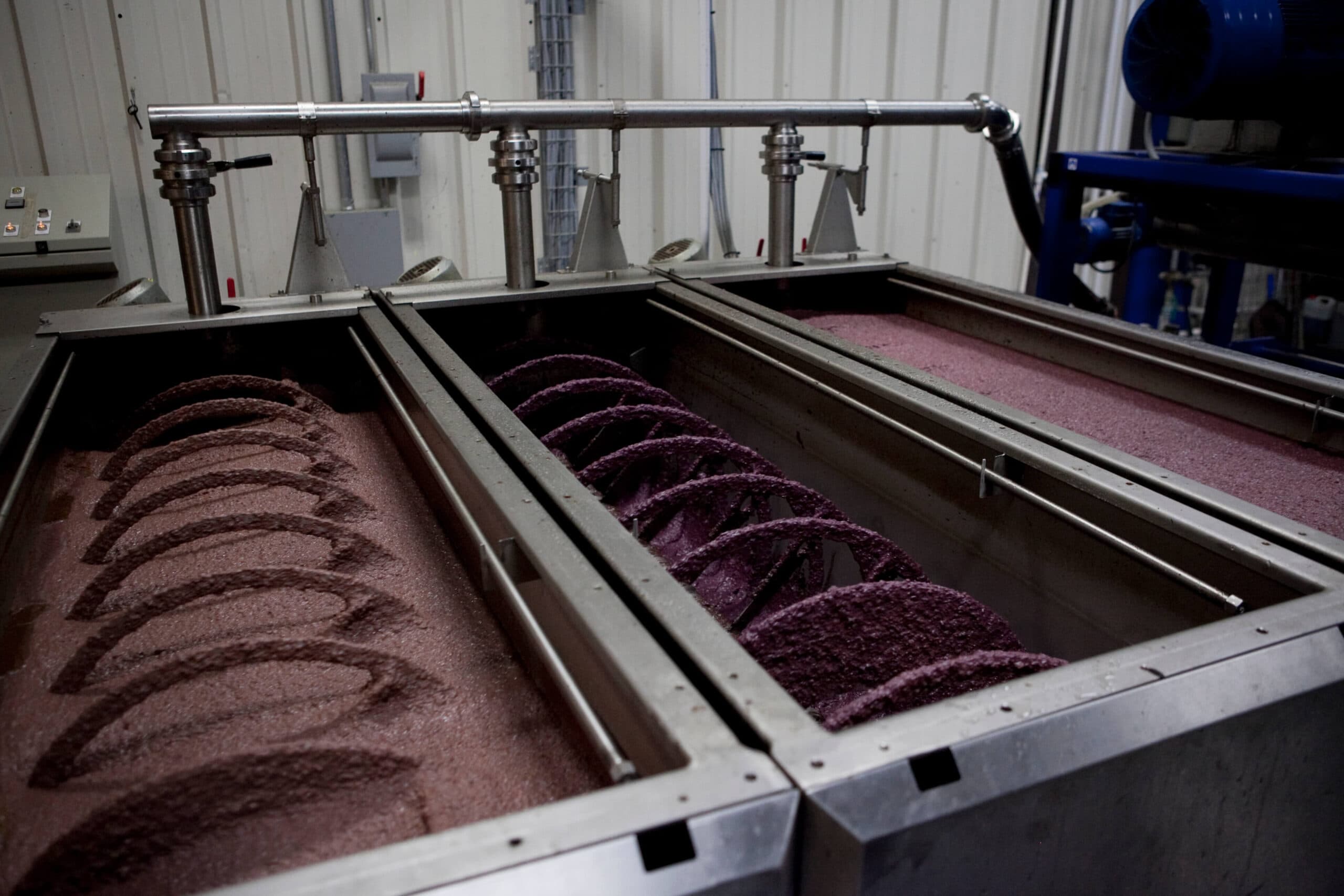 Industrial mixing equipment with rotating augers in two long metal tanks containing a purple substance.