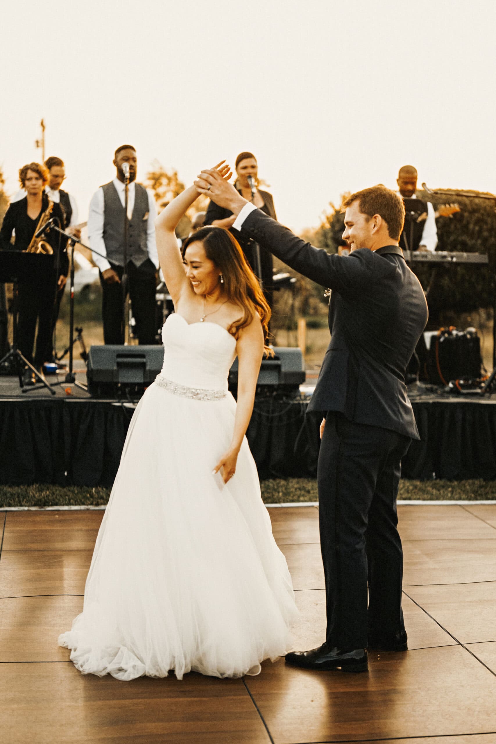 A bride and groom dance joyfully together on their wedding day, with a live band performing in the background.