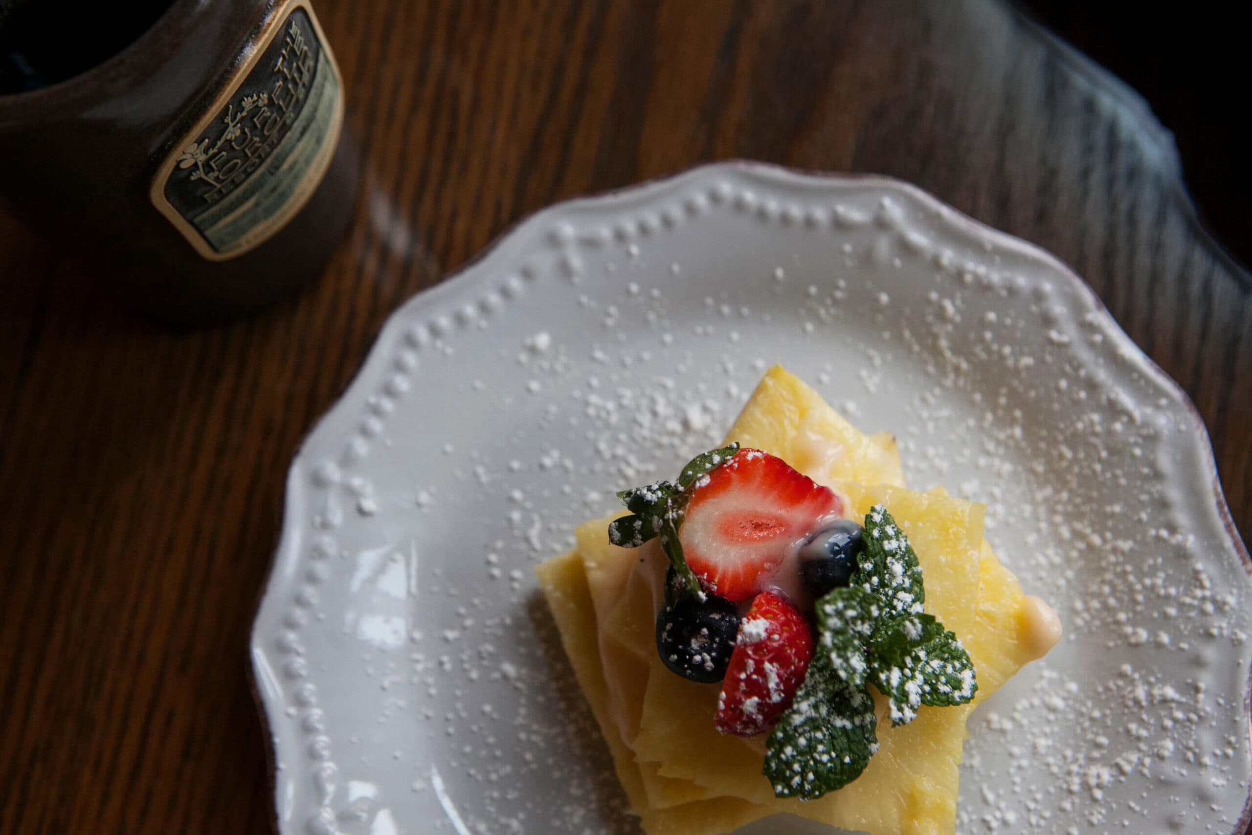 A stacked dessert topped with fresh berries and mint, sprinkled with powdered sugar on a decorative plate.