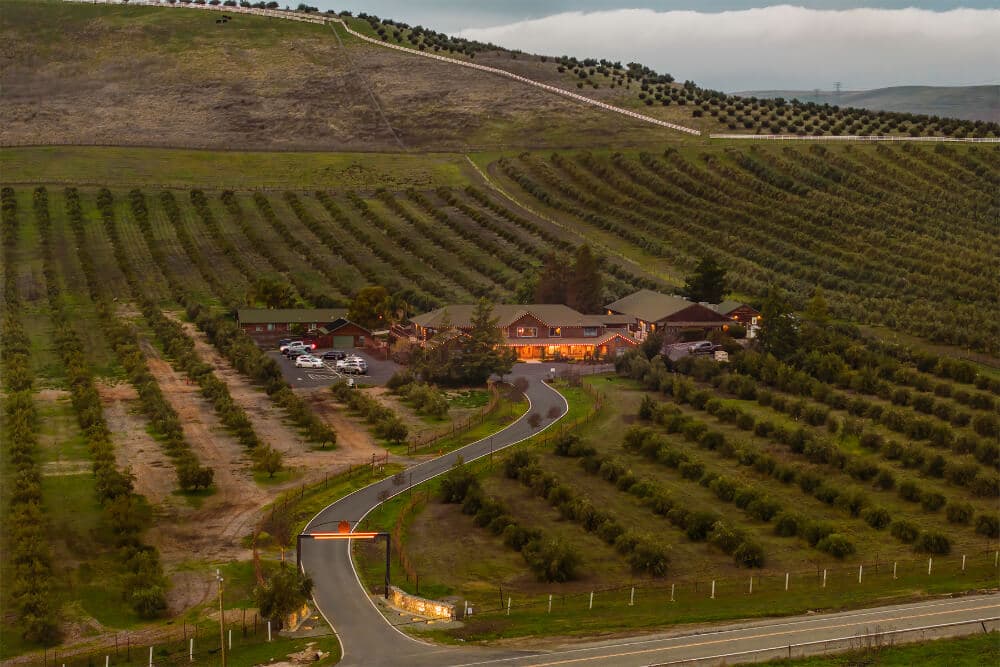 Aerial view of a rustic lodge nestled among lush orchards and rolling hills.