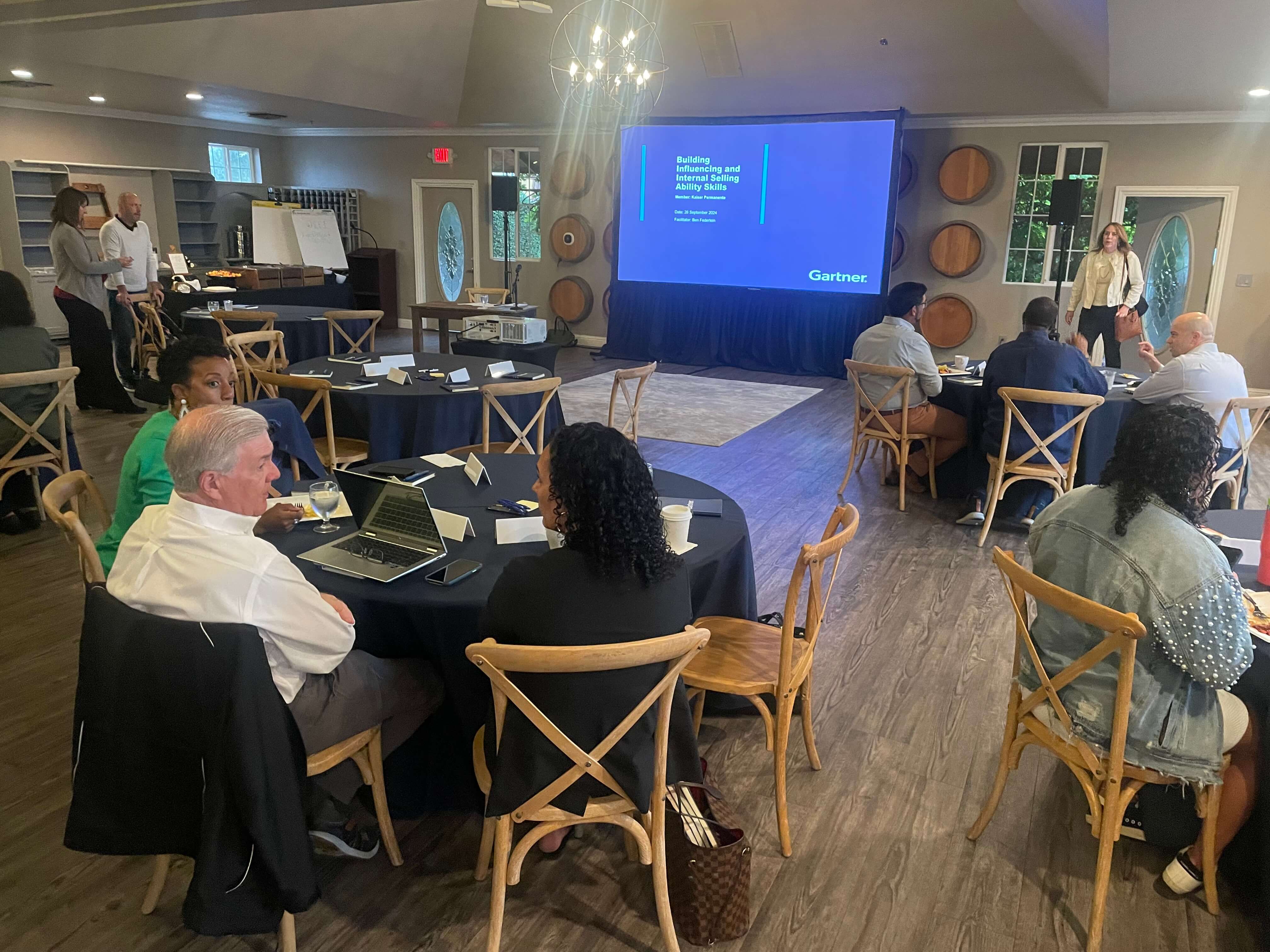 Conference attendees engage in a meeting with a presentation visible in the background.