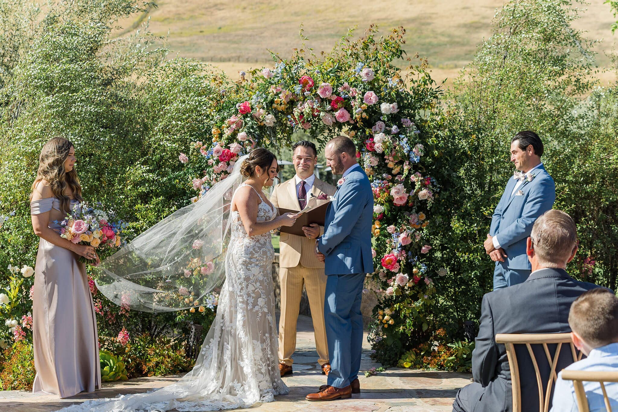 A couple exchanges vows under a floral arch during their wedding ceremony.