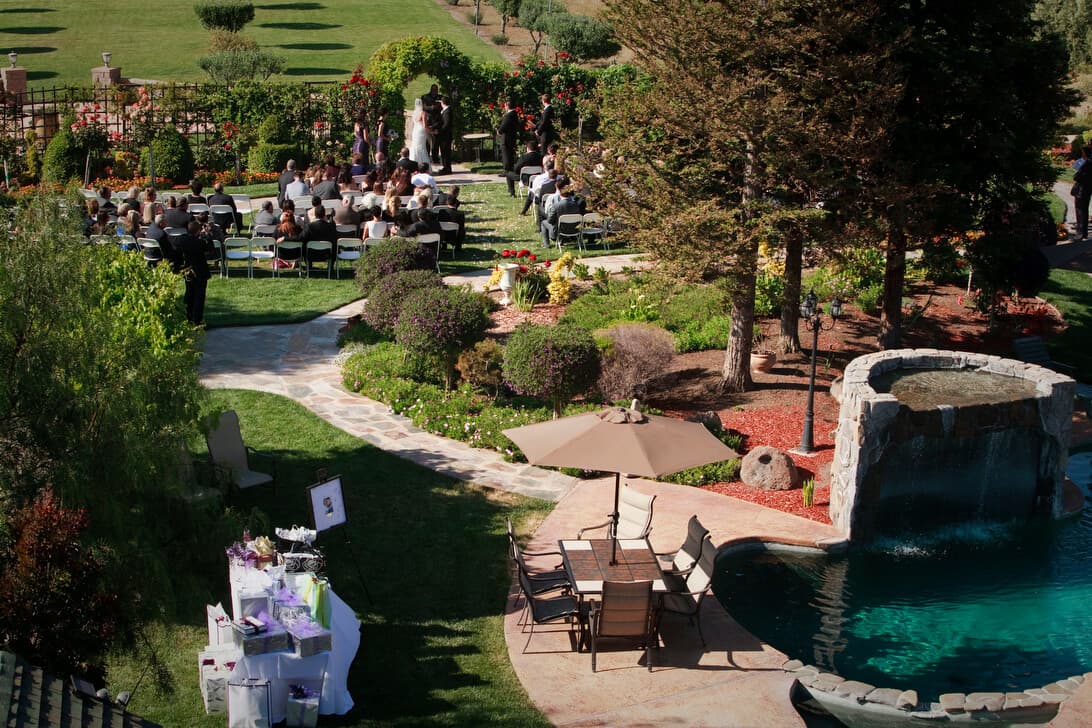 Aerial view of a wedding ceremony in a lush garden setting with guests seated and a waterfall pool nearby.