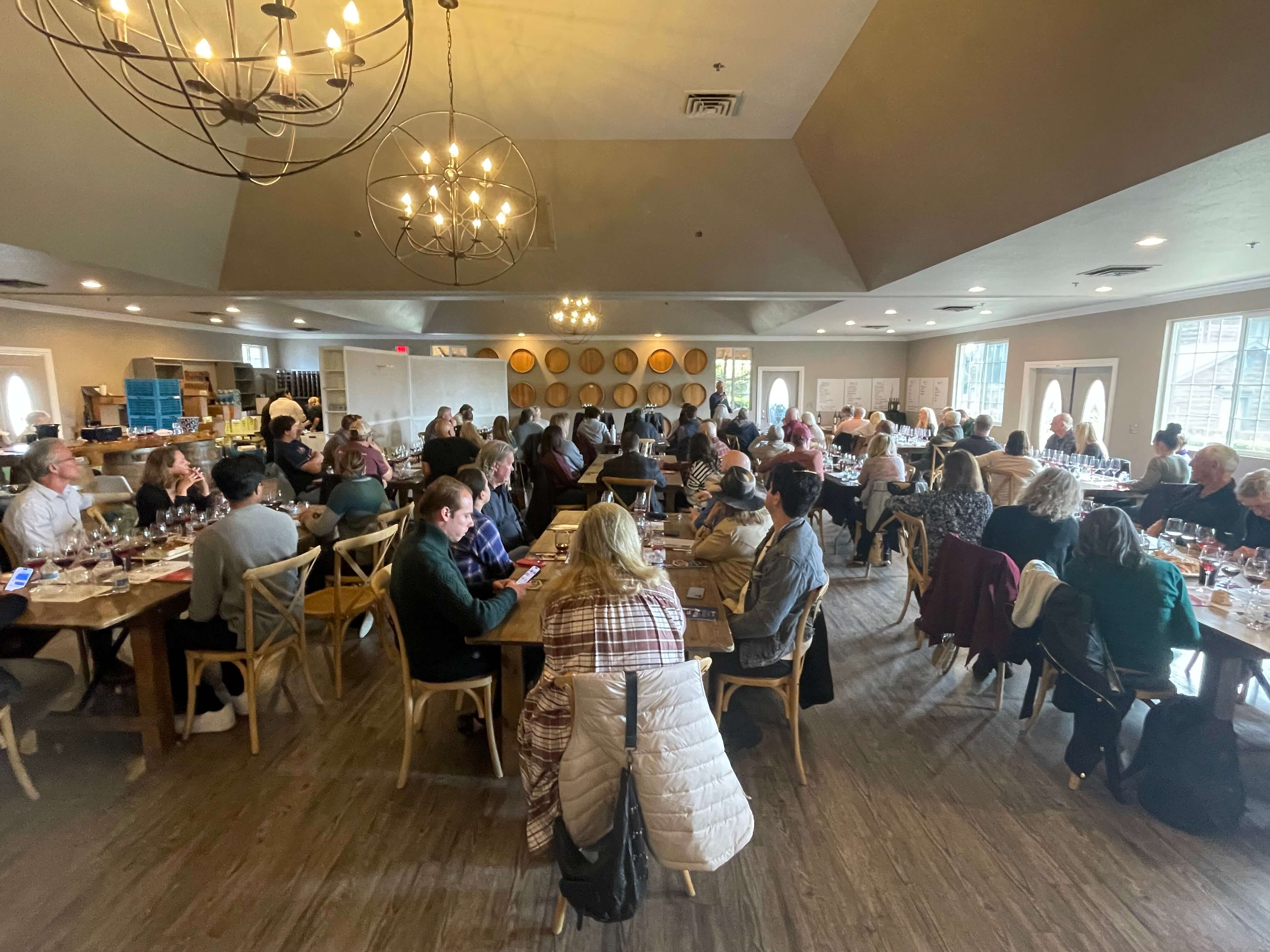 A large group of people seated at tables in a spacious, well-lit wine tasting room.