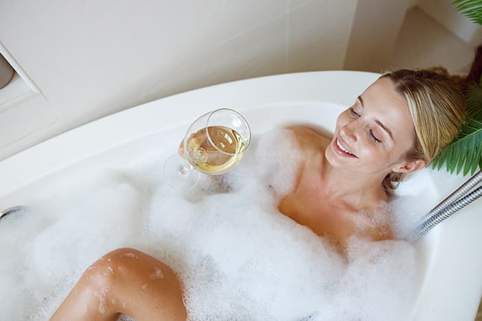 A woman relaxes in a bubble bath while holding a glass of wine.